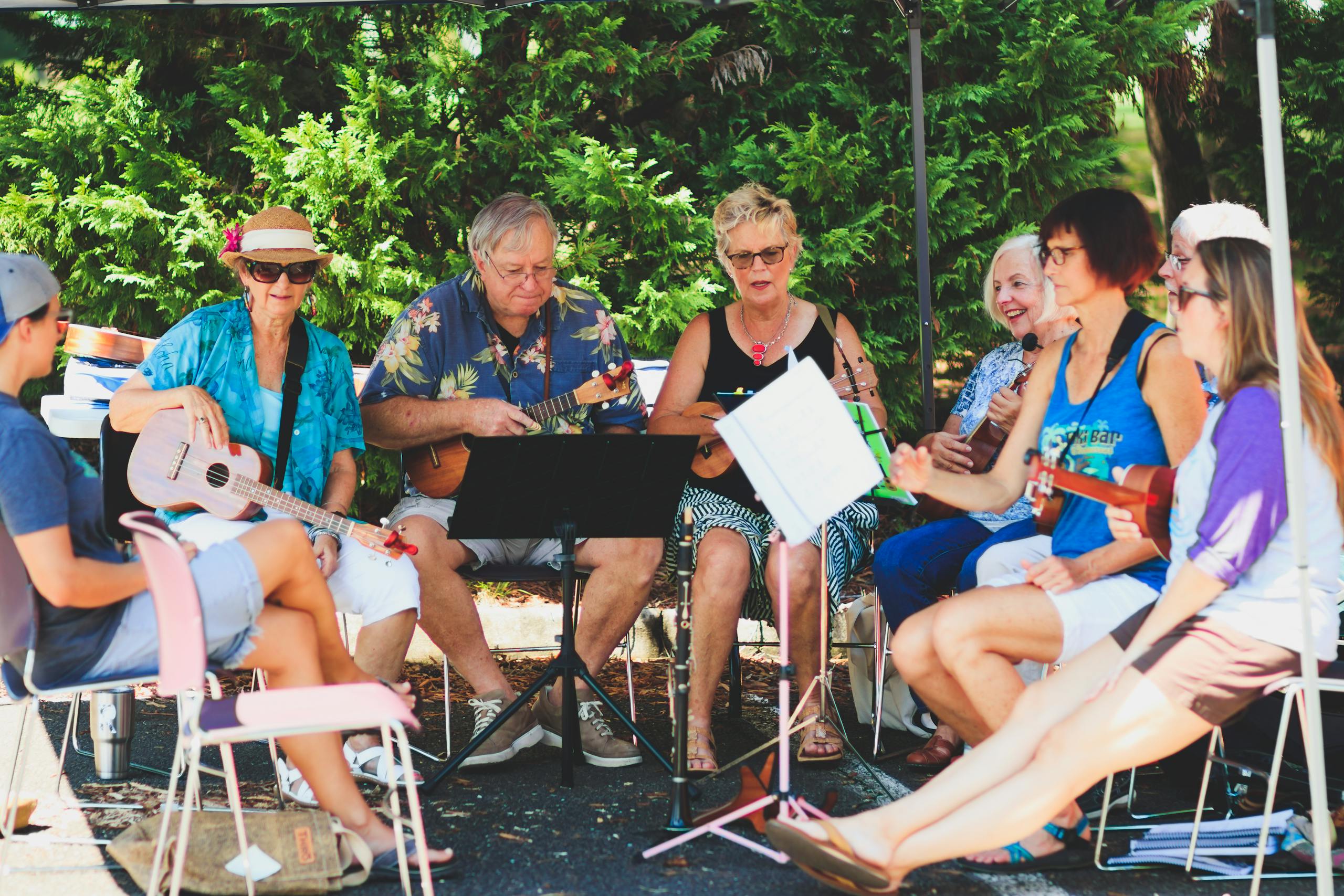 A cheerful group of adults playing ukuleles outdoors under a canopy.